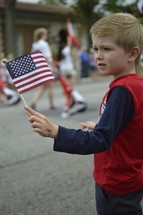 a young boy holding an American flag at a parade 