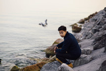 man sitting on rocks by the ocean 