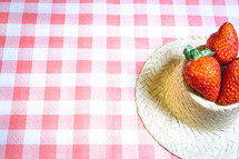 Fresh strawberries decorated on a straw hat. on a red picnic blanket.