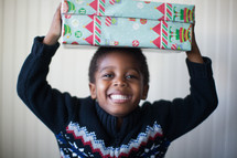 a boy child holding a Christmas present over his head 