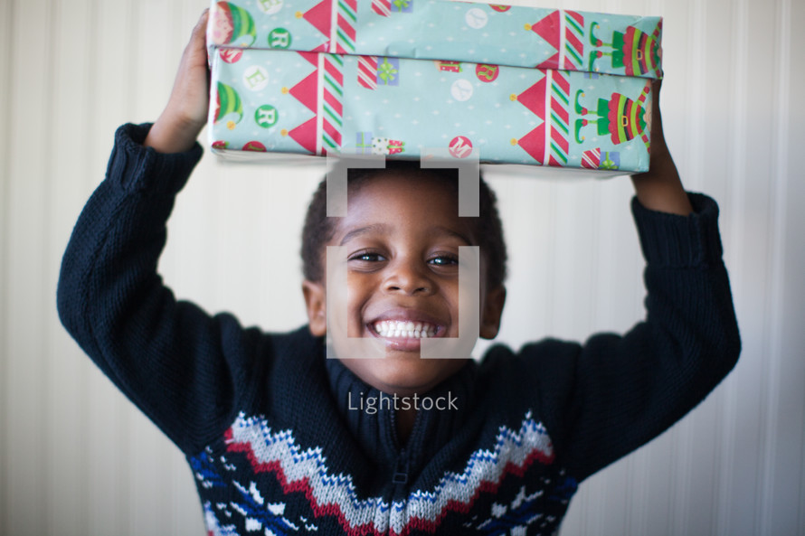 a boy child holding a Christmas present over his head 