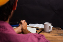 man with praying hands over a journal and an open Bible 