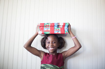 a girl child holding a wrapped gift over her head 