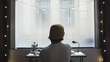 man at a desk looking out a window in an apartment 