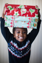 a boy child holding wrapped Christmas gifts over his head 