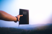 raised hand holding the holy Bible. background with blue sky in morning. copy space.