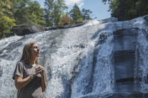 woman standing in front of a waterfall in Asheville, NC with praying hands 