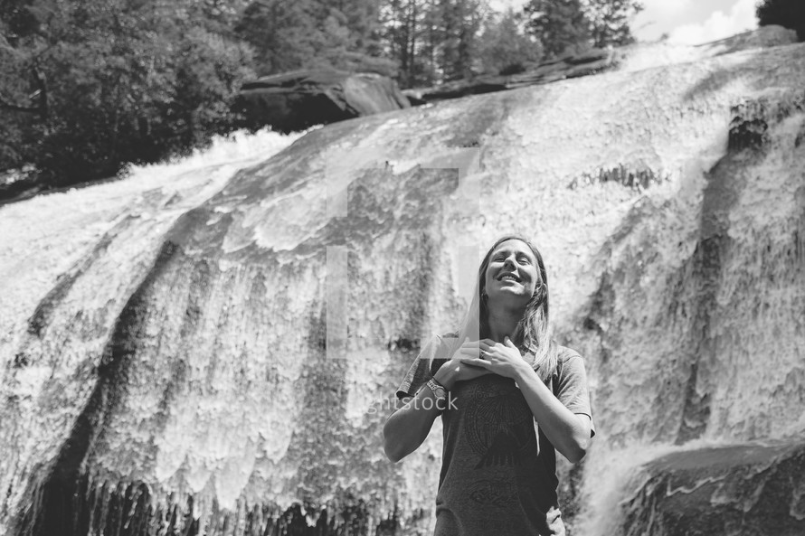 woman with her hands over her heart in front of a waterfall 
