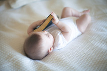 Infant girl laying on a bed holding a Bible.