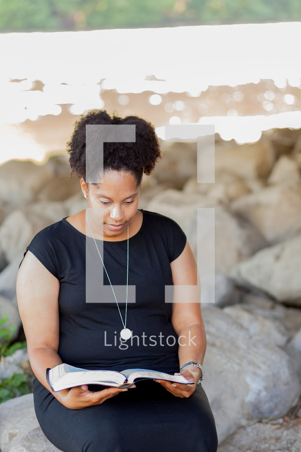 an African American woman sitting reading a Bible outdoors