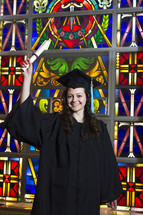 graduate holding up her diploma in front of a stained glass window