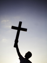 Silhouette of man holding cross with one hand in the air over his head.