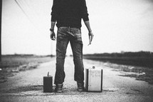 man standing next to suitcases looking down a road holding a Bible