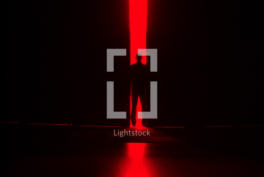 Man standing in a doorway with bright red light behind.