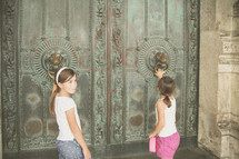 children knocking on front doors of an ancient cathedral 
