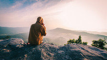 man sitting at the top of a mountain looking out at the view 
