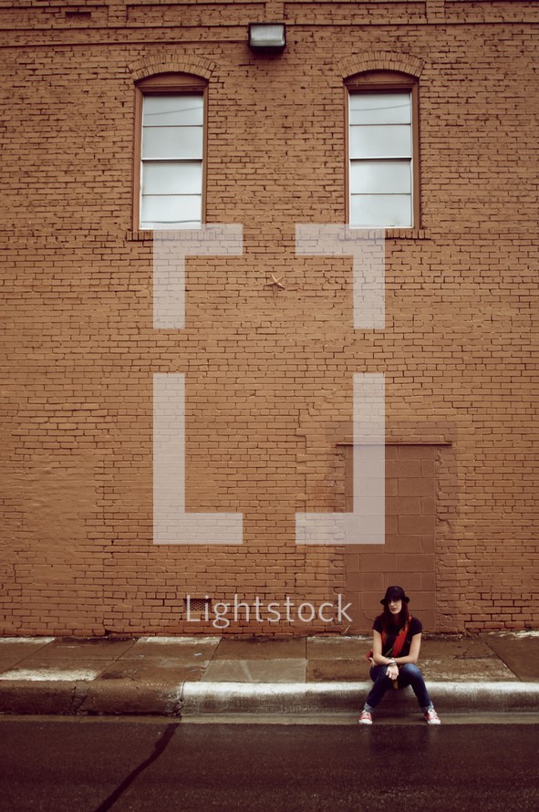 Girl sitting on a sidewalk in front of a brick building