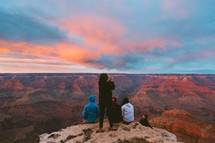 people sitting at the edge of a cliff overlooking a canyon at sunset 