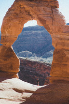 a man standing under a red rock arched rock formation 