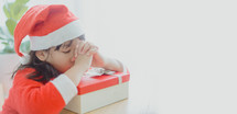 a little girl in a Santa suit praying over a Christmas gift 