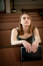 A woman holding a Bible sitting in a church pew looking to God 