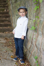 Young boy leaning against a stone vine covered wall, stairs in the background