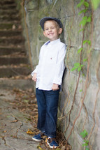 A smiling boy leaning against a rock wall.