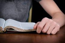 Teen reading the Bible on a wood table.