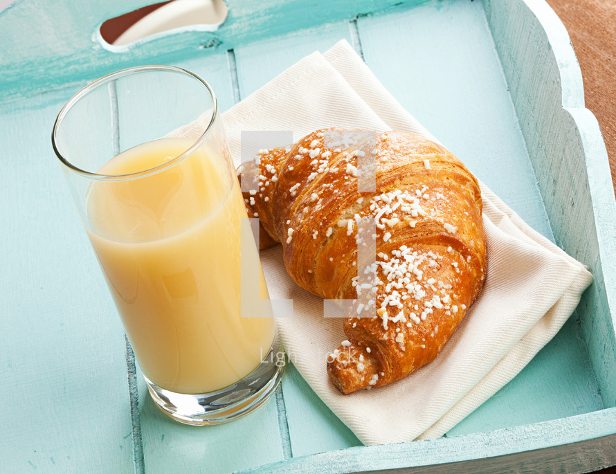 Croissant and pear juice on light green tray.