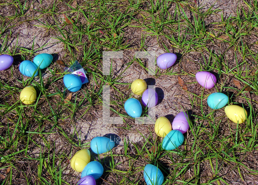 A green field with pastel colored Easter eggs including blue, purple, aquamarine blue, green and yellow greet kids going on an Easter egg hunt at a local church ground during the Easter holiday. 