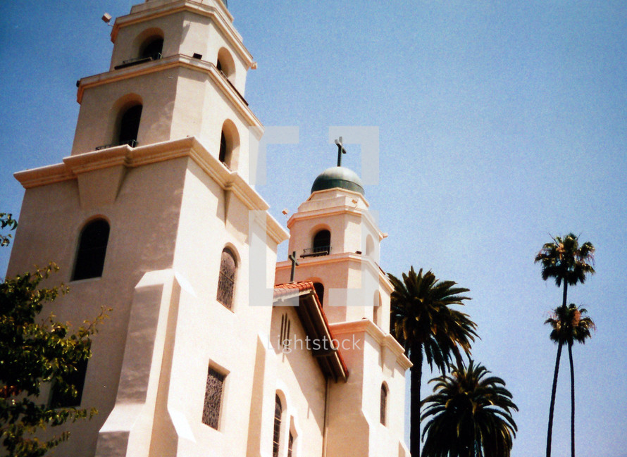 A Spanish styled Mission church in Sunny southern California surrounded by tropical Palm Trees against a clear blue sky. 