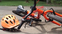 An orange bicycle and helmet in the driveway with a bat and soccer ball