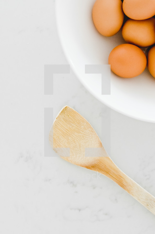 brown eggs in a white bowl and wooden spoon 