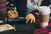 woman wearing a sweater with hearts holding a coffee cup writing Valentines cards 