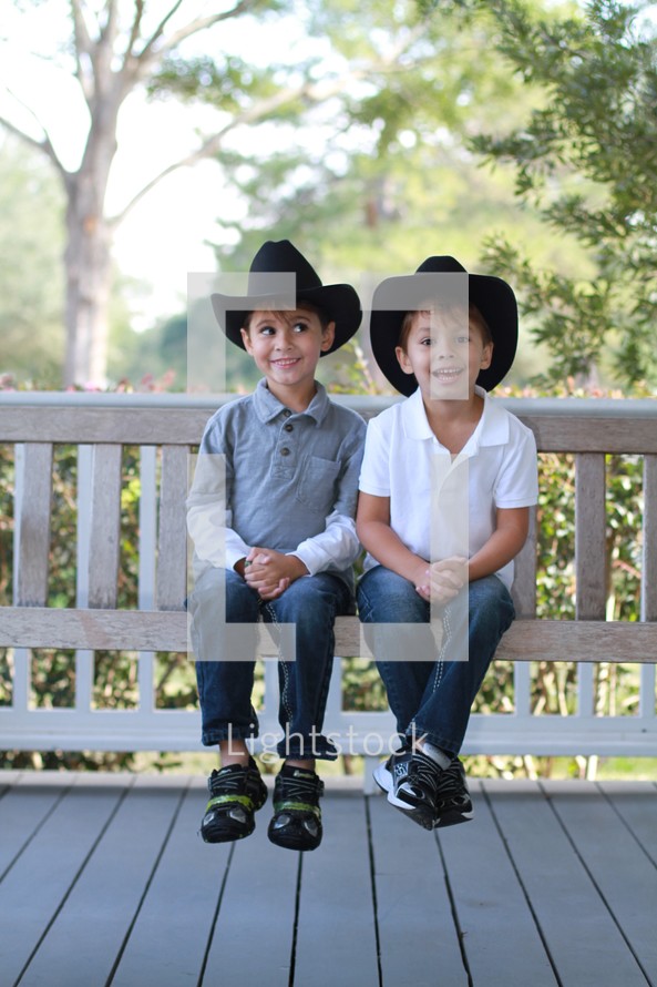 Young brothers sitting on a porch swing wearing cowboy hats