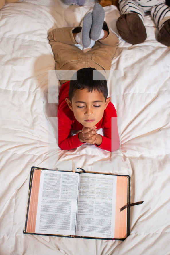 child praying over a Bible in bed