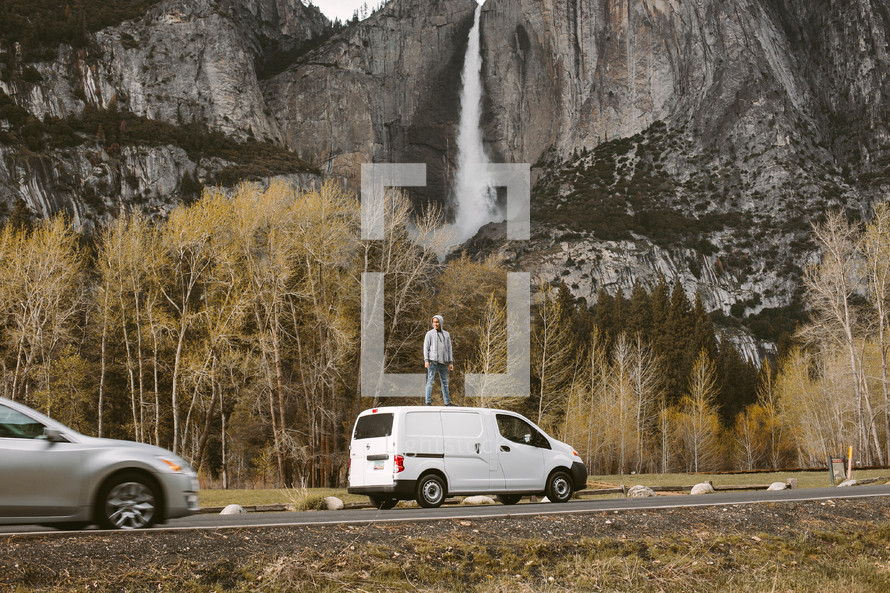 man standing on the roof of a van with a waterfall in the background in Yosemite 