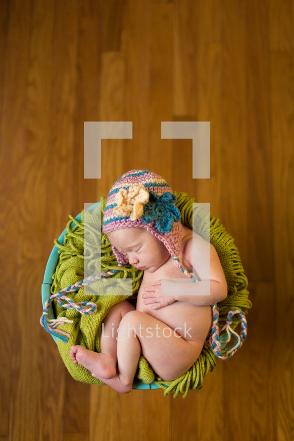 naked newborn in a basket wearing a hat