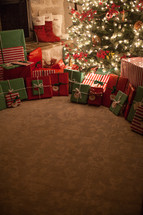 gifts under a Christmas tree and stockings by a fireplace 