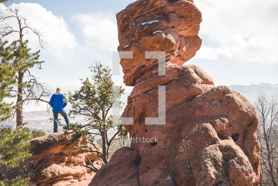 man standing on a red rock formation at the top of a mountain 