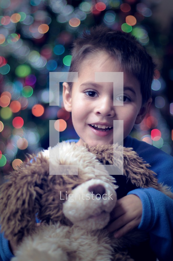 Little boy snuggling a stuffed animal  in front of a Christmas tree