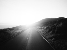 A glaring sun shines on a road leading through the countryside.