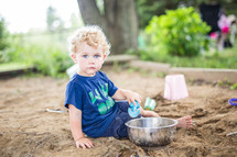 toddler boy playing in a sand box 