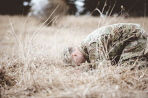 soldier kneeling in a field praying 