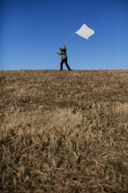 Man carrying white flag on grassy hilltop.