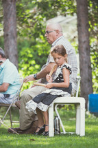 a grandfather sitting outdoors with his granddaughter 