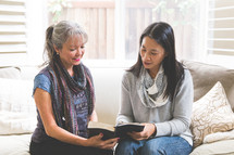 Asian women sitting on a couch reading a Bible 