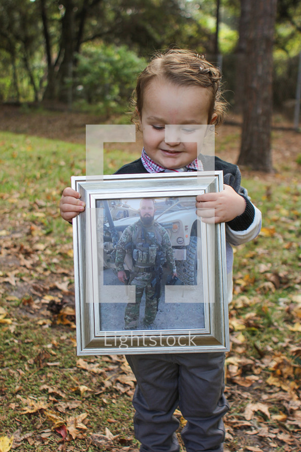 Boy standing in the woods holding a framed photo of his soldIer father.