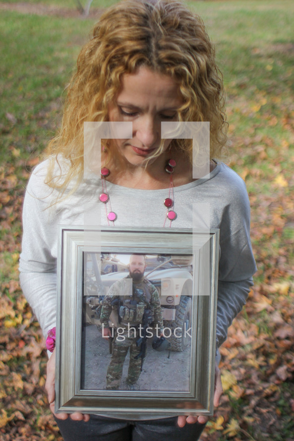 Woman, looking down at a picture of a soldier in camouflage