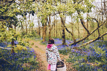 a girl walking on a path in the woods carrying a picnic basket 